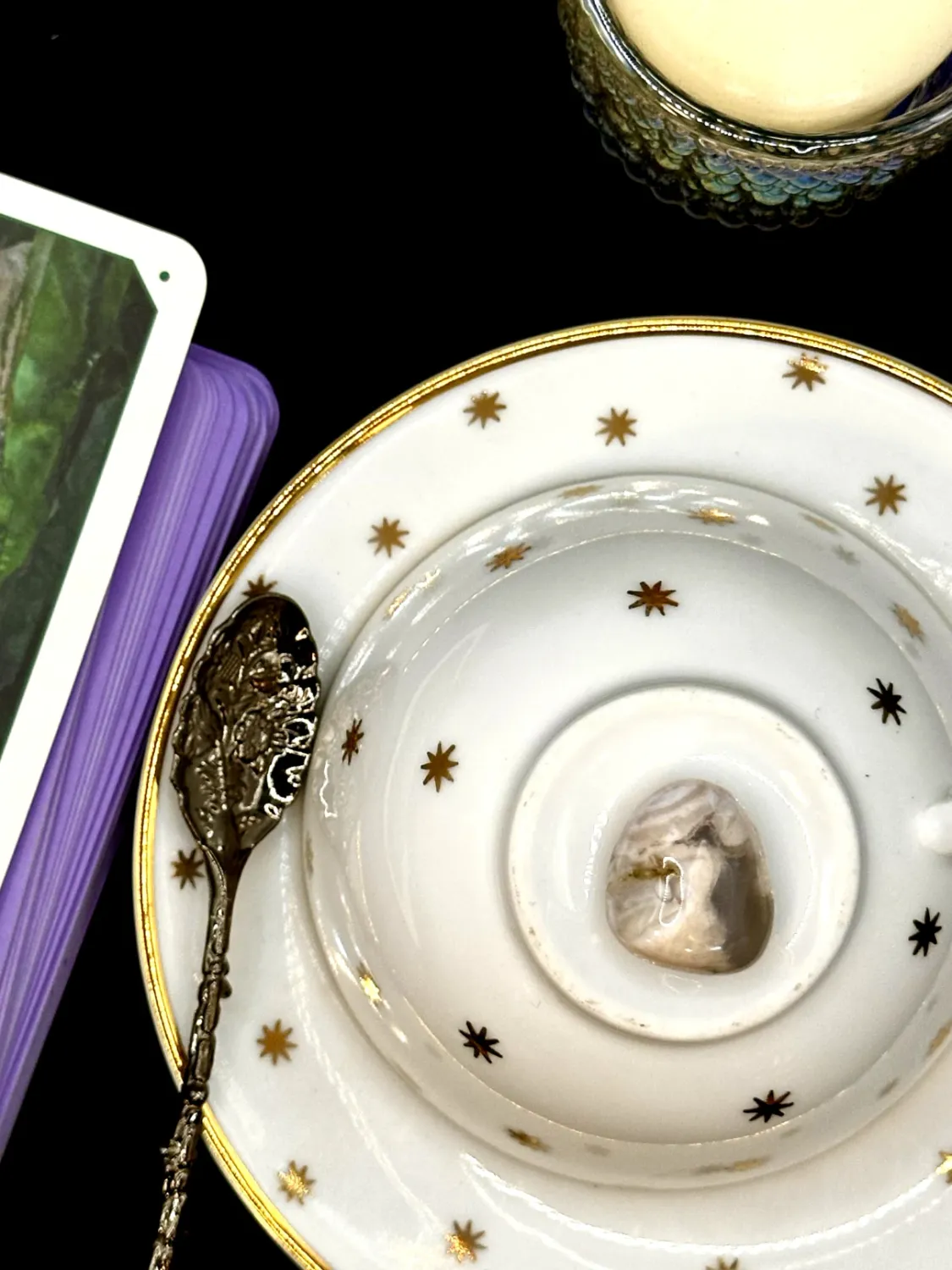 Flower agate tumbled stone in cream and gray with white plume patterns on a white teacup and saucer with gold stars.