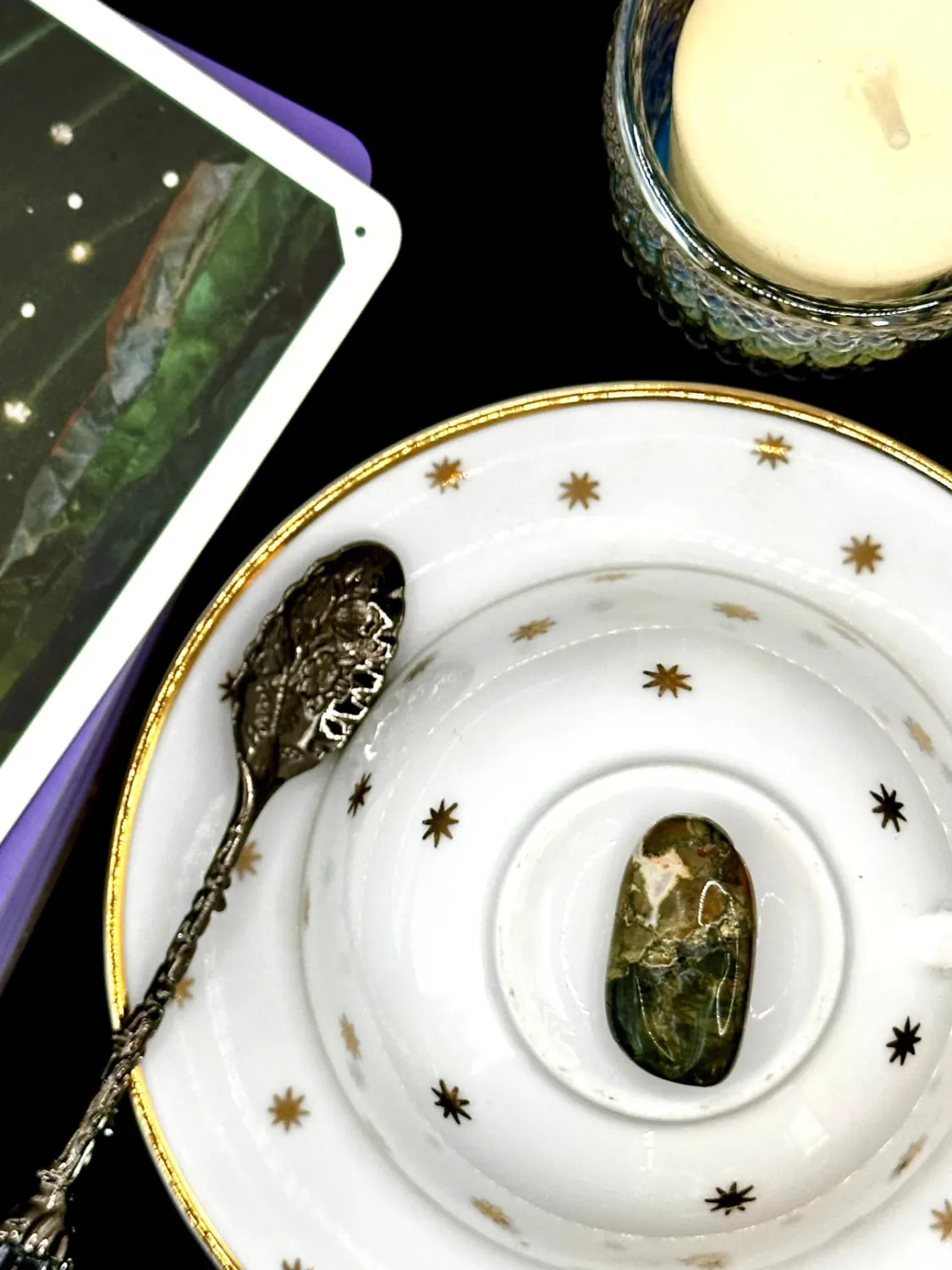 Rainforest jasper tumbled stone in mossy green with tan and peach patches on a white teacup and saucer with gold stars.