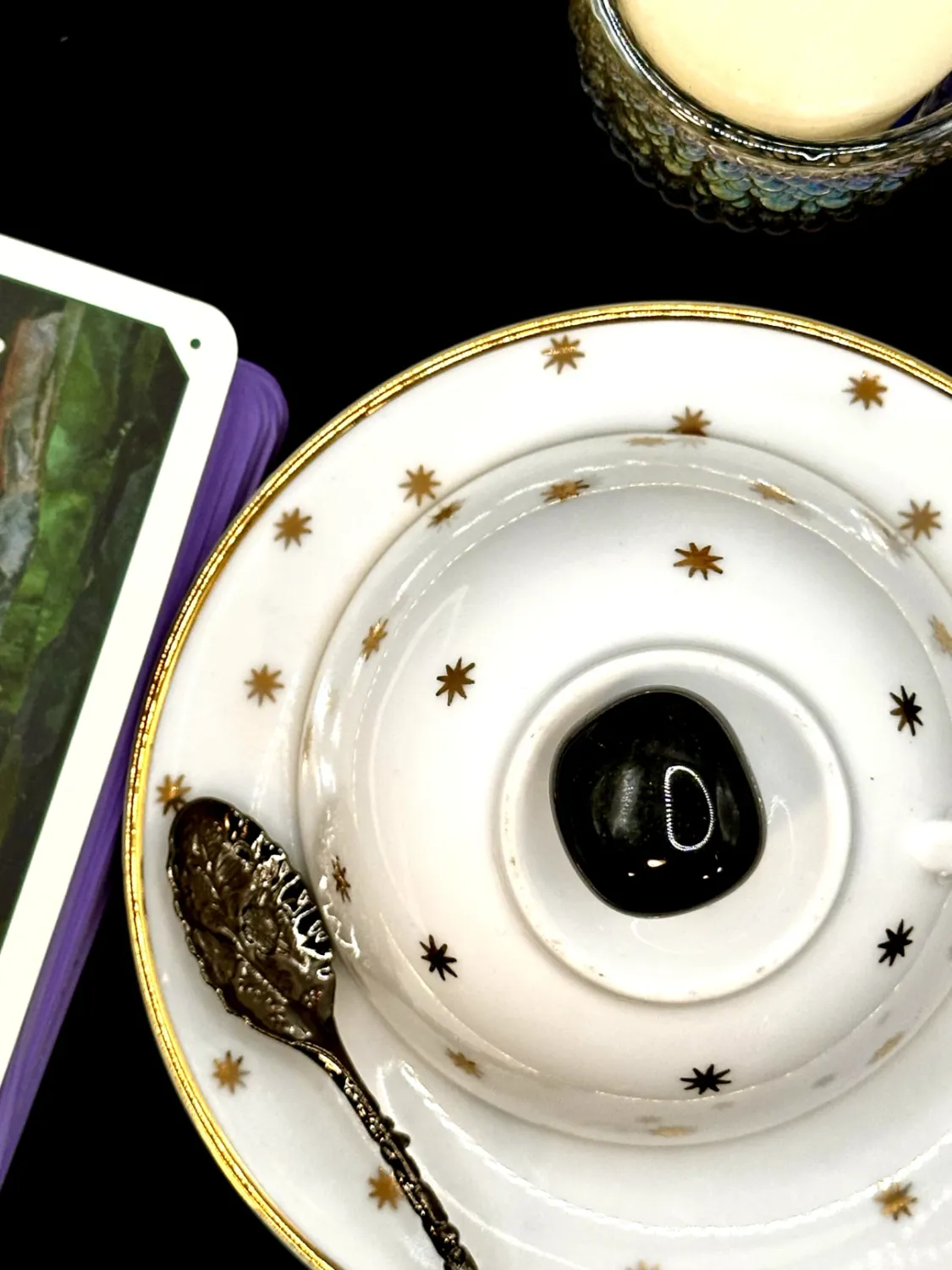 Glossy black obsidian tumbled stone on a white teacup and saucer with gold stars.
