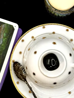 Glossy black obsidian tumbled stone on a white teacup and saucer with gold stars.