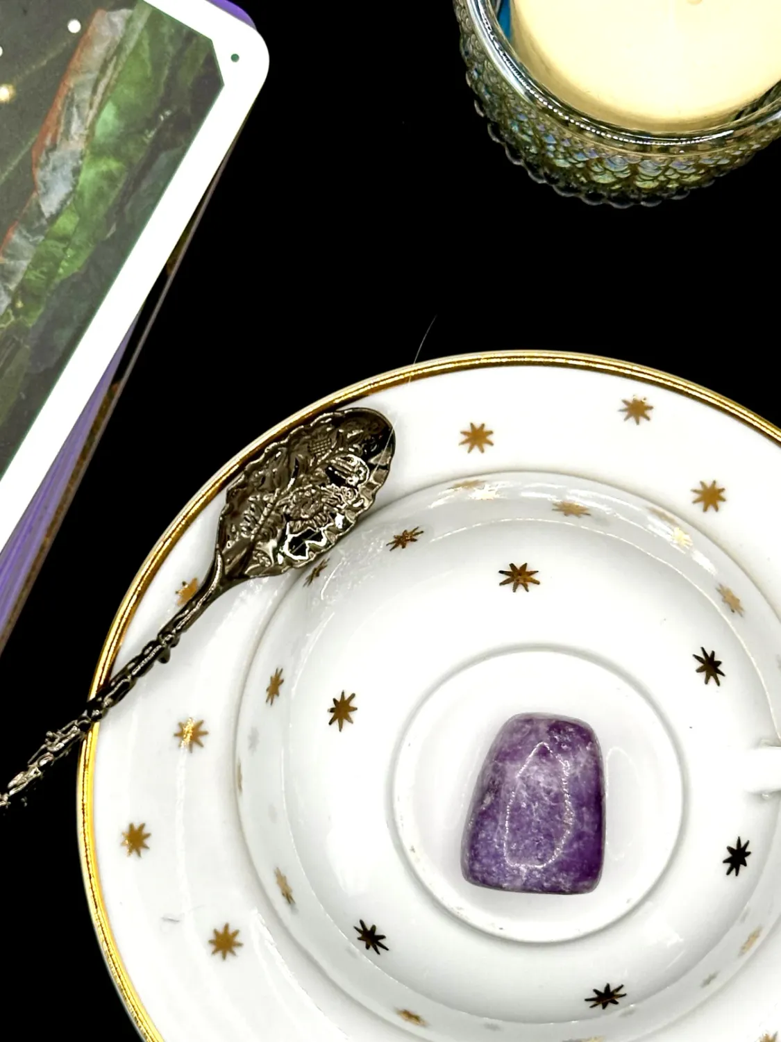 Purple lepidolite tumbled stone with white flecks on a white teacup and saucer with gold stars.