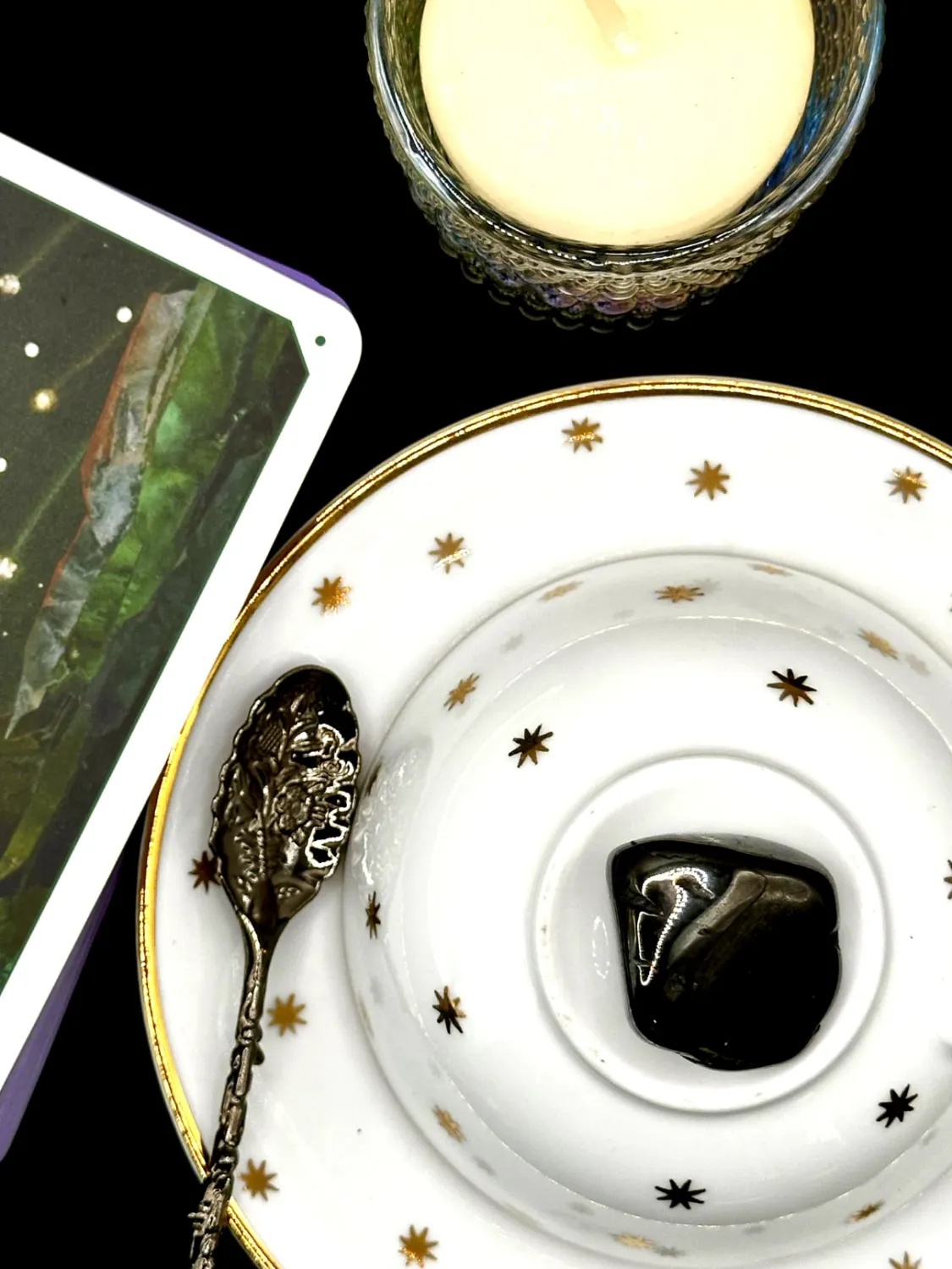 Glossy black jet tumbled stone with angled faces on a white teacup and saucer with gold stars.
