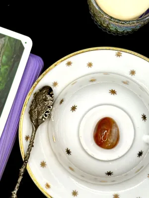 Fiery orange and red fire agate tumbled stone on a white teacup and saucer with gold stars.