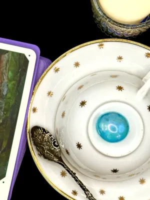 Bright aqua aura tumbled stone with an iridescent, glassy shine on a white teacup and saucer with gold stars.