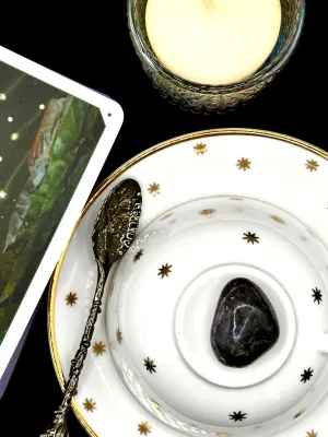 Deep indigo iolite tumbled stone on a white teacup and saucer with gold stars.