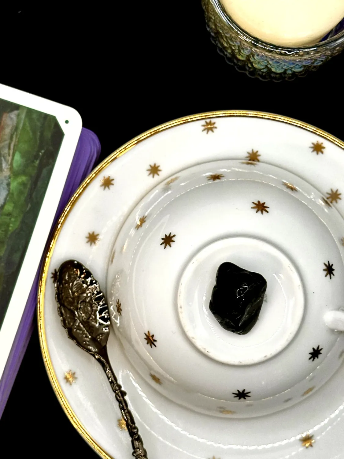 Black tourmaline tumbled stone with a glossy, ridged surface on a white teacup and saucer with gold stars.