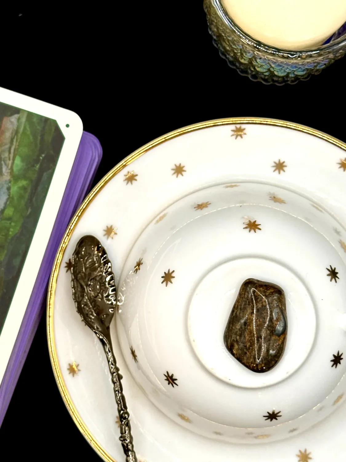 Brown bronzite tumbled stone with a bronze shimmer on a white teacup and saucer with gold stars.