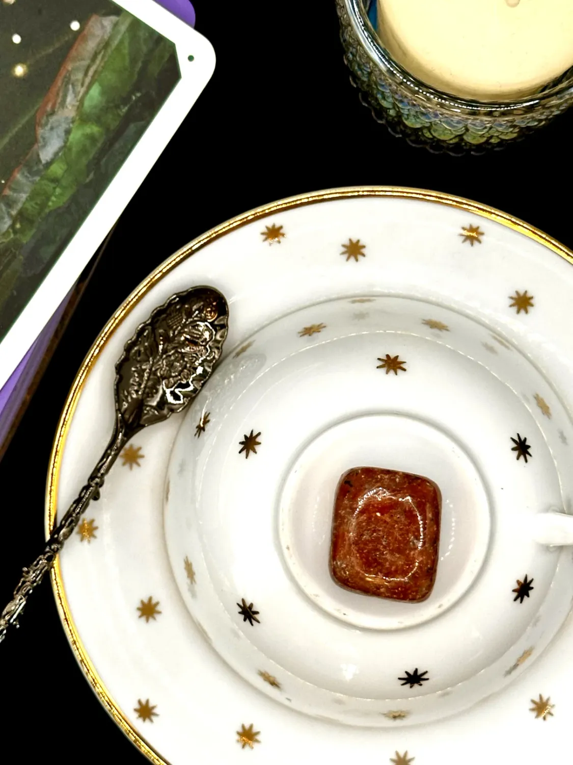 Orchid calcite tumbled stone mottled in orange and red with white flecks on a white teacup and saucer with gold stars.