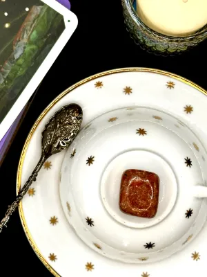 Orchid calcite tumbled stone mottled in orange and red with white flecks on a white teacup and saucer with gold stars.