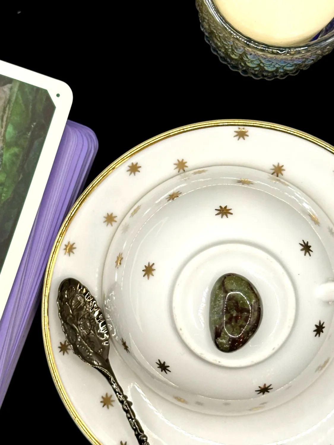 Dragons blood jasper tumbled stone in mossy green with dark red patches on a white teacup and saucer with gold stars.