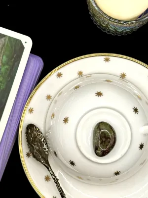 Dragons blood jasper tumbled stone in mossy green with dark red patches on a white teacup and saucer with gold stars.