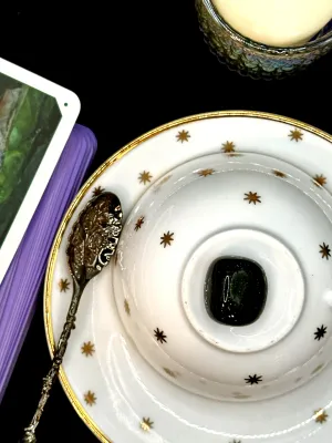 Very dark green goldstone tumbled stone flecked with glitter on a white teacup and saucer with gold stars.
