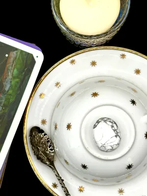White howlite tumbled stone with gray veining on a white teacup and saucer with gold stars.