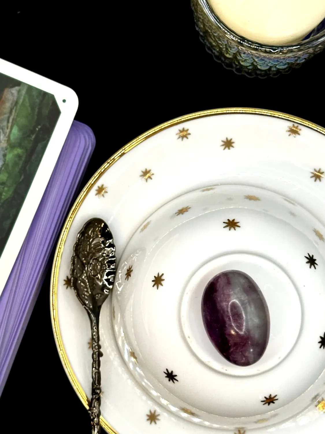Oval purple fluorite tumbled stone with a pale band on a white teacup and saucer with gold stars.