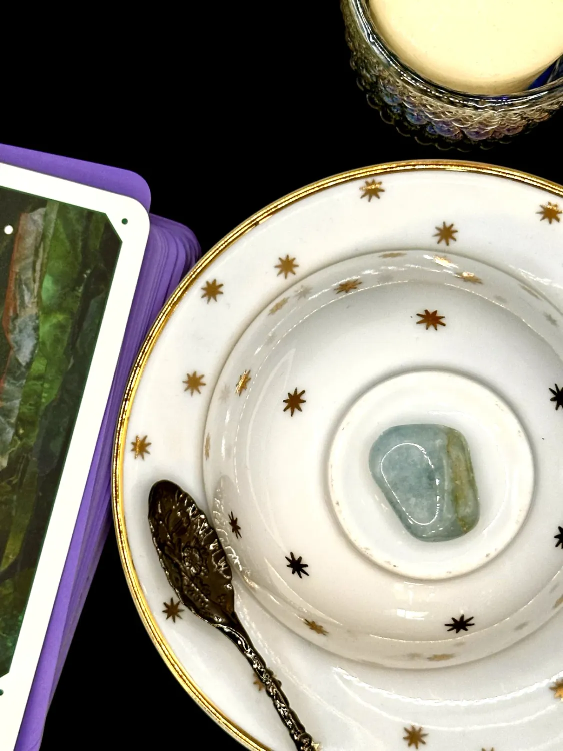 Pale blue-green aquamarine tumbled stone with soft white clouding on a white teacup and saucer with gold stars.