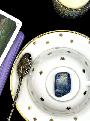 Blue kyanite tumbled stone with white and silver streaks on a white teacup and saucer with gold stars.