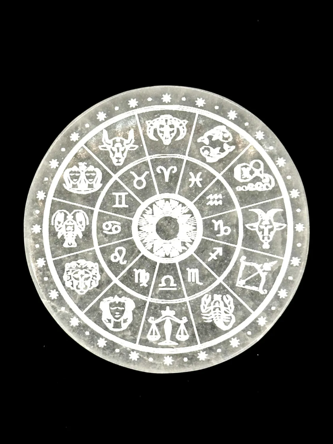 Round white selenite plate engraved with a wheel of the twelve zodiac signs, on a black background.