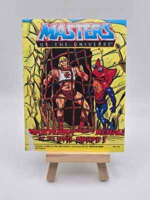Front cover of the English version of the vintage &#39;Masters of the Universe&#39; mini comic titled &#39;Mantenna and the Menace of the Evil Horde!&#39; displayed on a small wooden easel. The cover features He-Man trapped in a net with Mantenna standing beside him. Some wear is visible on the bottom left corner.