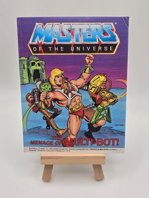 Front cover of the vintage &#39;Masters of the Universe&#39; mini comic titled &#39;The Menace of Multi-Bot!&#39; displayed on a small wooden easel. The cover features He-Man battling the robotic Multi-Bot, with Castle Grayskull in the background.