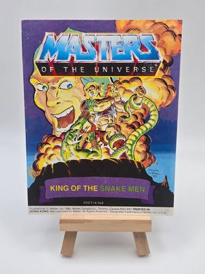 Front English cover of the 1985 &#39;King of the Snake Men&#39; - Mini Masters of the Universe (MOTU) Vintage Comic Book by Mattel, displayed on a small wooden easel, showcasing vibrant artwork of He-Man and King Hiss.