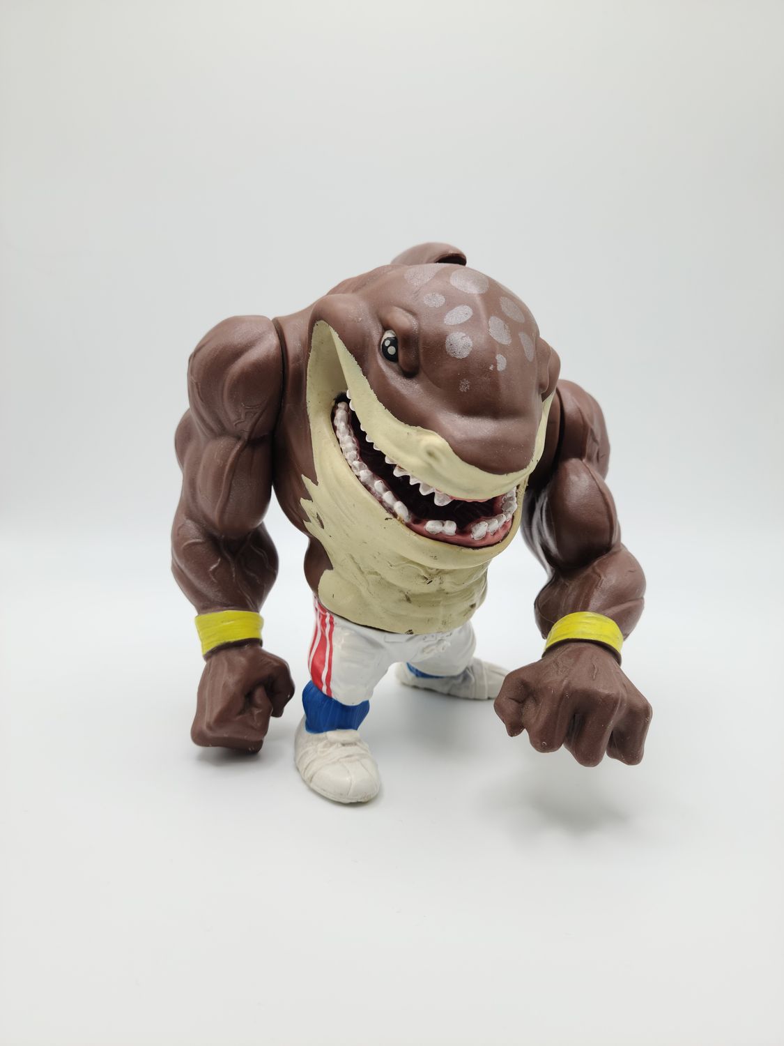 Front view of the 1994 Big Slammu (yellow sweat wrist bands) Street Sharks vintage action figure made by Mattel standing on a flat surface.