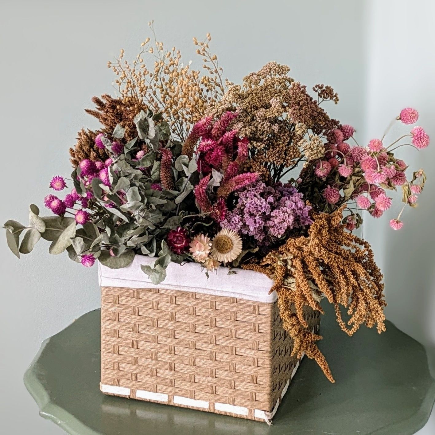 Brown basket of dried flowers on a green table with a white background.