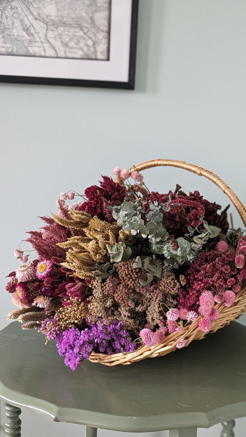 Basket of pink, white, and green dried flowers on a green table with a white background.