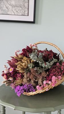 Basket of pink, white, and green dried flowers on a green table with a white background.