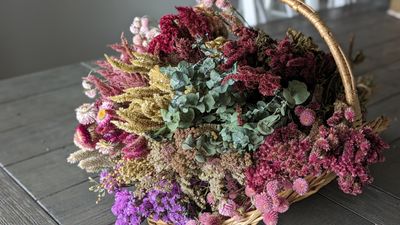Basket of pink, white, and green dried flowers on a green table with a white background.