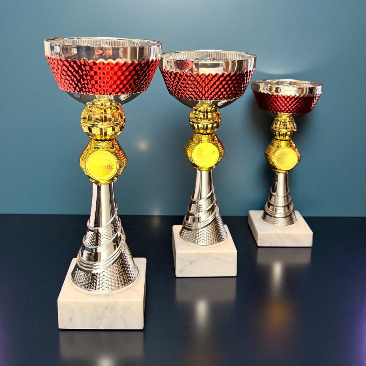 3er-Pokalserie „Trinity Champion“ mit roter strukturierter Schale, gold  & silberfarbenem Korpus und hellem Marmorsockel