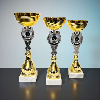 3er-Pokalserie „Kratzspitz“ mit goldfarbener Schale, silbernem Emblemträger und hellem Carrara-Marmorsockel