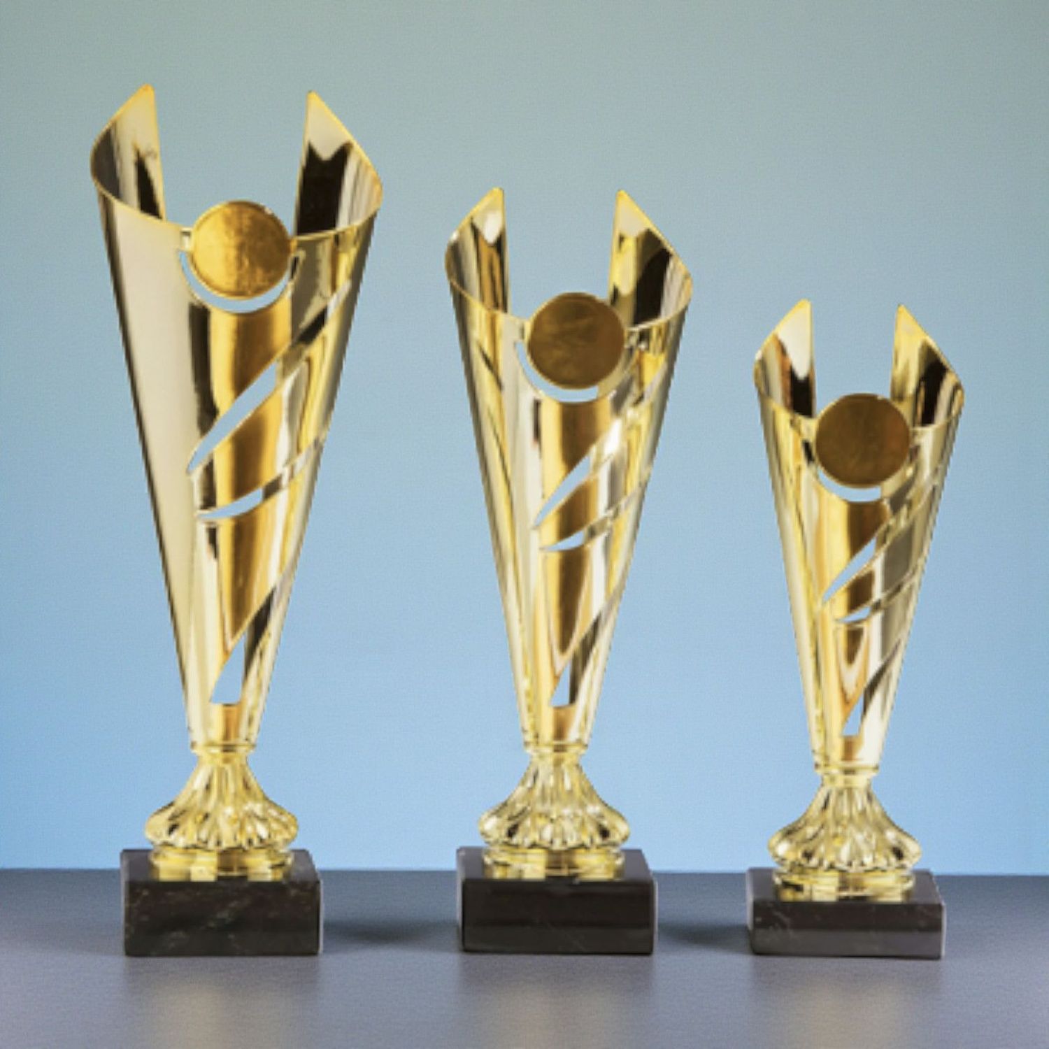 Luxus-Metallpokal Thiema in Gold mit geschwungenem Design, rundem Emblemträger und schwarzem Marmorsockel