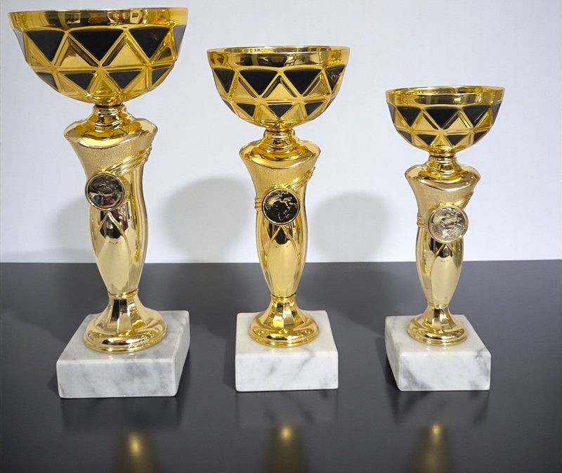 Drei Pokale der Serie ROSE mit schwarz-goldfarbener Schale, goldfarbenem Pokalkörper mit Emblemhalter und Marmorsockel in unt