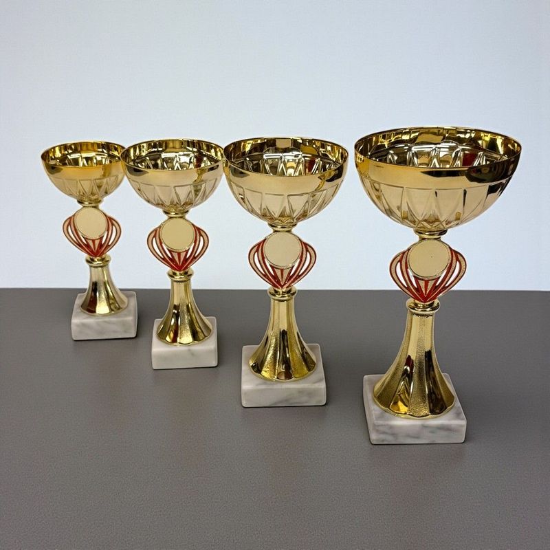 Pokal „Triton“ im 4er-Set mit goldfarbener Metallschale, rotem Zierelement im Mittelteil, rundem Emblemträger und weißem Marm