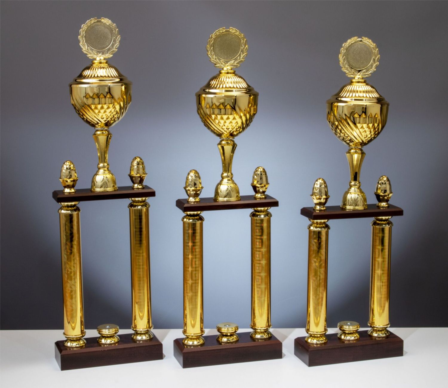 Säulenpokal Dakota in Goldoptik mit klassischem Kelch, goldfarbenen Säulen und Holzsockel, erweiterbar mit Figuren, 3 Größen