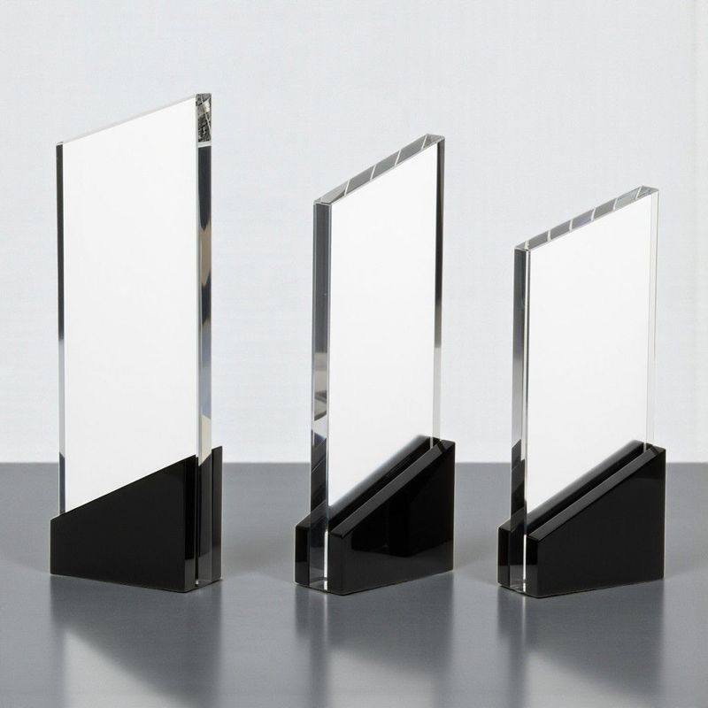 Klare Glastrophäe mit schwarzem Sockel und kantiger Form auf graublauem Hintergrund.