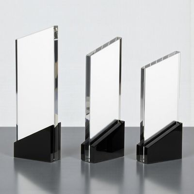 Klare Glastrophäe mit schwarzem Sockel und kantiger Form auf graublauem Hintergrund.