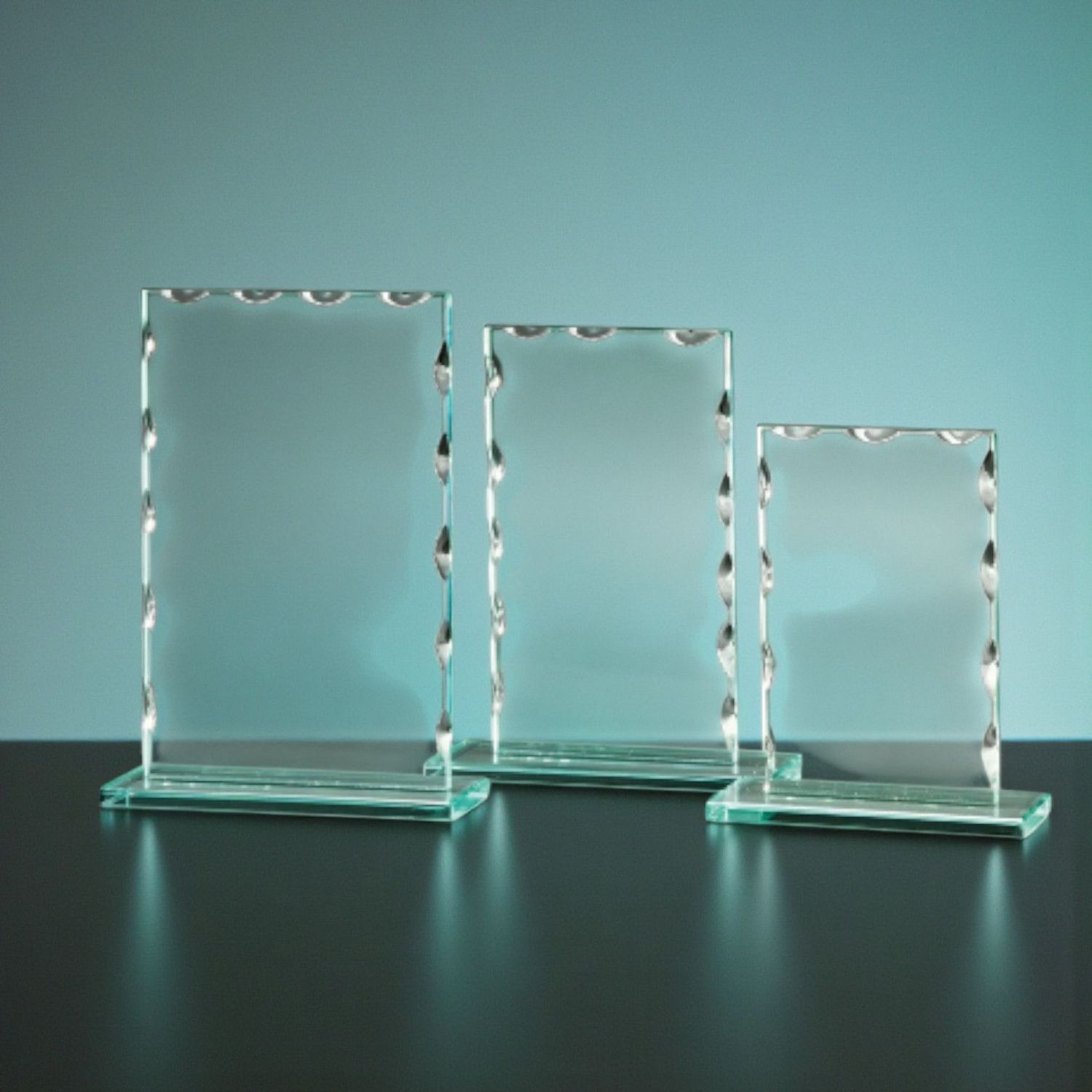 Drei klare Glastrophäen mit Wellenschliff und Glasfuß auf dunklem Untergrund, unterschiedliche Höhen, Studioaufnahme.