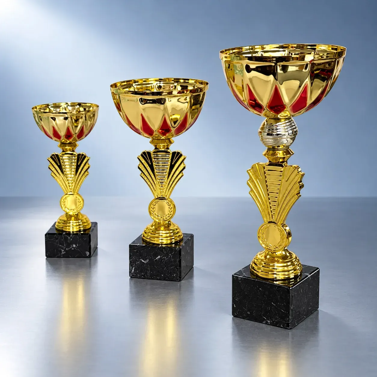 Pokal Goldstar Red, ab € 6,00 Drei goldfarbene Kinderpokale mit roten Akzenten, Emblemträgern und schwarzen Marmorsockeln in 19, 21 und 23,5 cm Höhe.