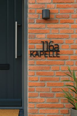 Naambord voordeur zwart RVS met huisnummer en familienaam gemonteerd met afstandshouders aan de achterkant naast voordeur