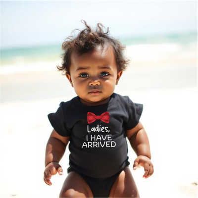 Mini Boss – Ladies I Have Arrived Black Baby Romper Baby wearing a black romper with the playful text ‘Ladies, I Have Arrived’ on the front.