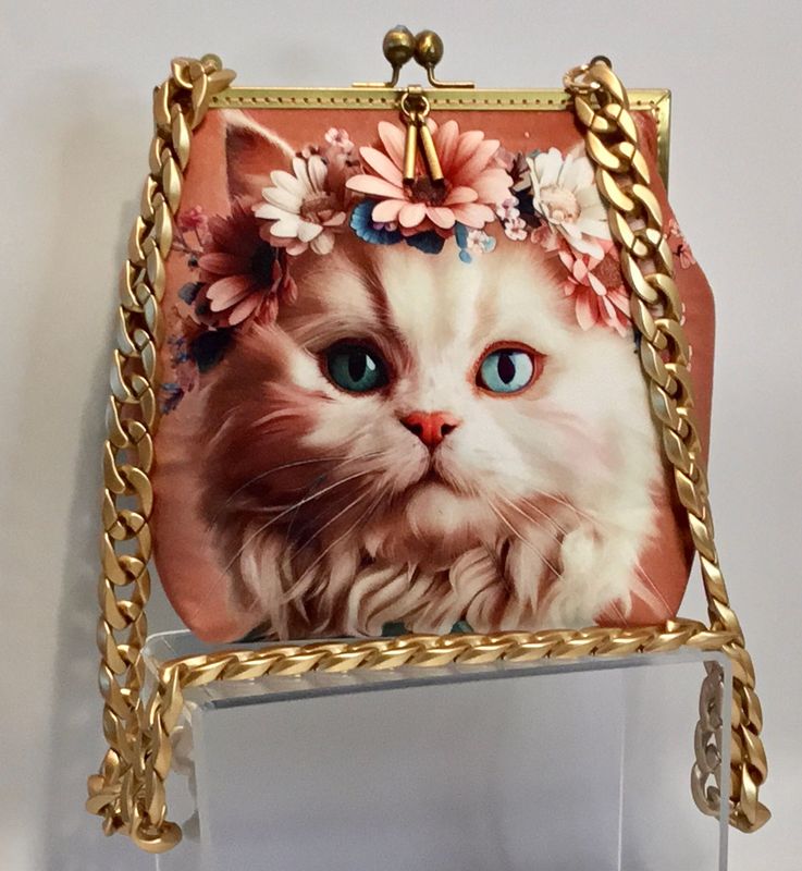 Bolso con cara de gatita con corona de flores en terciopelo sintético , el forro tiene dos bolsillos uno d ellos con cremallera, la cadena es de resina,  la  boquilla es metálica cosida a mano, las medidas son 22de AL X28AN X8FON,