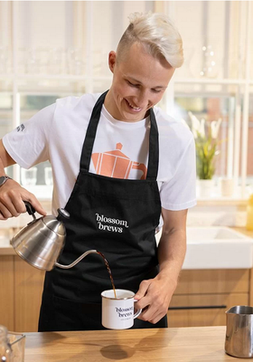 Mann in Schürze bereitet Kaffee in einer stilvollen, umweltfreundlichen Küche zu, symbolisiert nachhaltigen Lebensstil und individuelles Wohnen, angeboten von vilcom.shop.