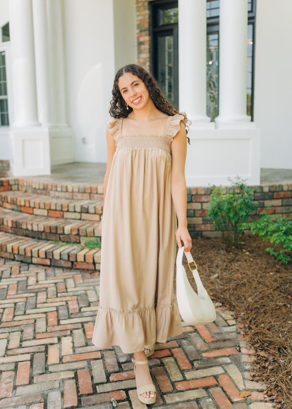 Model smiling while walking in beige smocked ruffle strap midi dress styled with wedges.