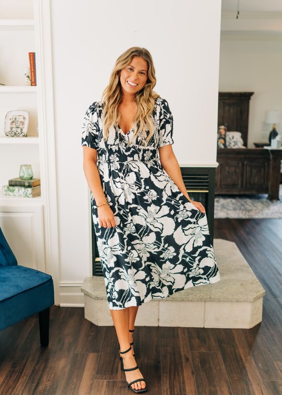 Woman wearing black and white floral smocked midi dress with short sleeves standing indoors.