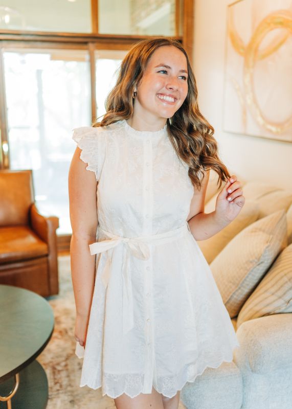 Close-up detail of flutter sleeves and lace embroidery on white mini dress.