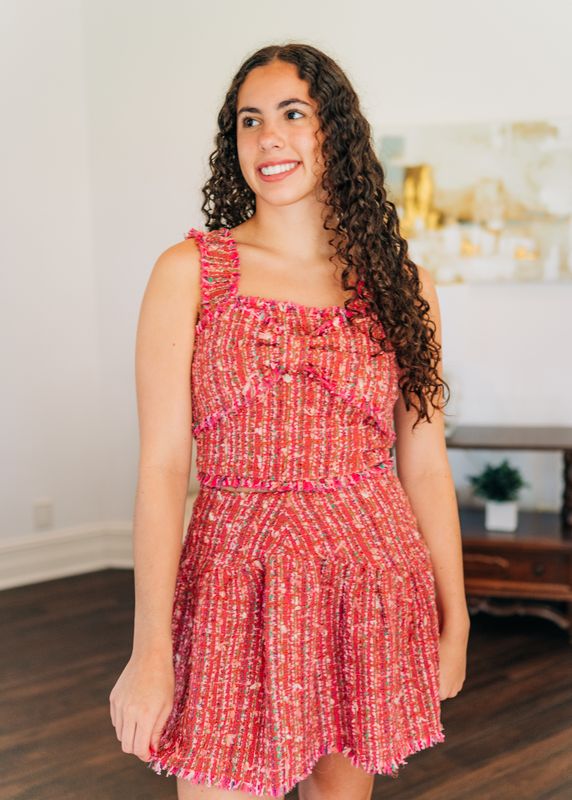 Model styled in pink tweed ruffle strap crop top and matching skirt set, smiling while standing in boutique-inspired setting.