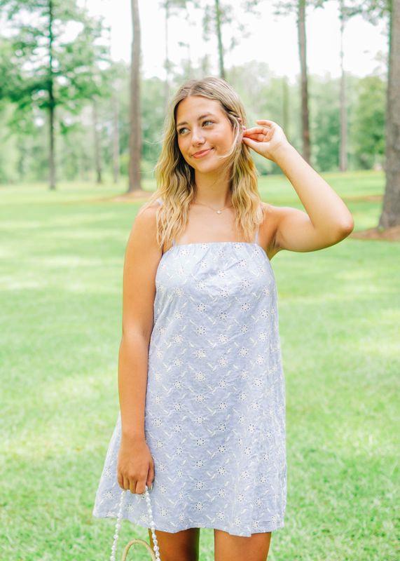 Close-up of woman wearing a light blue floral eyelet mini dress with spaghetti straps, smiling outdoors.