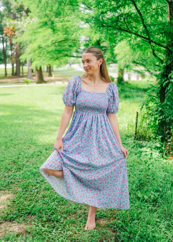 Front view of blue puff sleeve smocked maxi dress, model holding skirt with one hand while smiling.