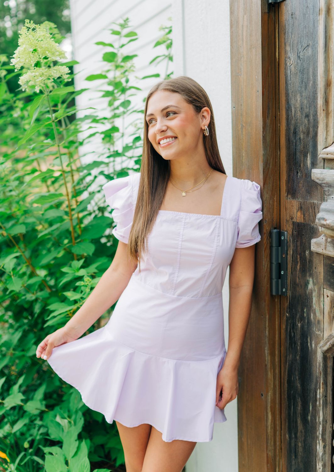 Woman posing in lilac square neck romper with puff sleeves, holding skirt overlay.